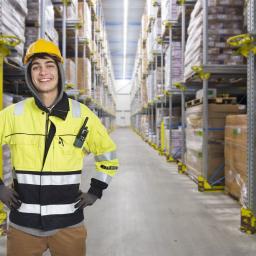 Ein junger Fachlagerist mit gelber Warnkleidung inmitten ein Hochregallagers