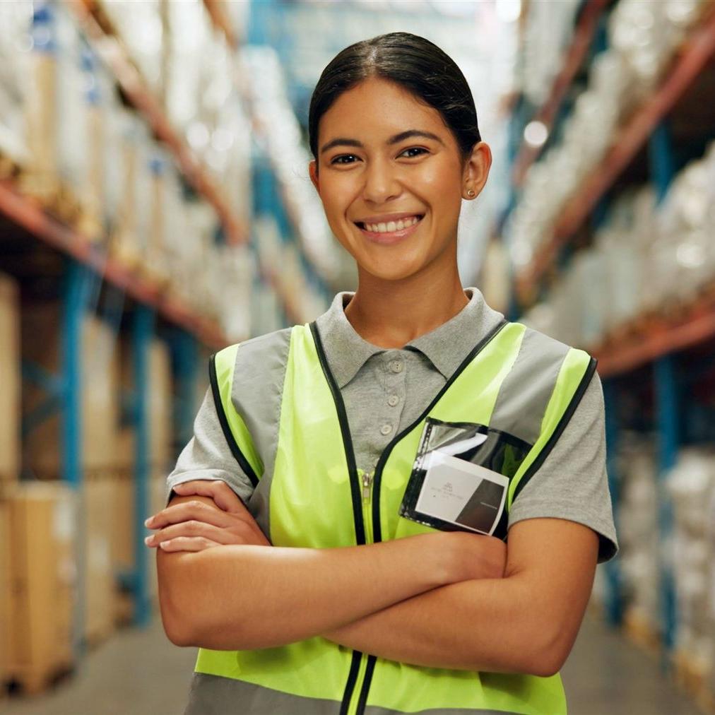 Eine junge Fachlageristin mit gelber Warnweste inmitten eines Hochregallagers