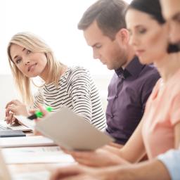 Eine Gruppe von Studenten sitzen arbeitend vor dem Laptop und eine Studentin lächelt direkt in die Kamera