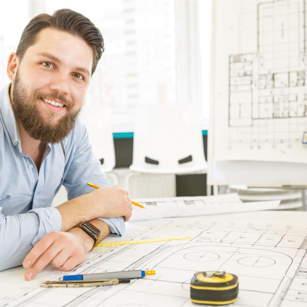 Ein junger Bauzeichner sitzt an seinem Schreibtisch