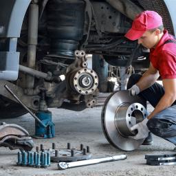 Ein junger Mechatroniker, knieend, wechselt die Bremsscheiben eines Lastkraftwagens